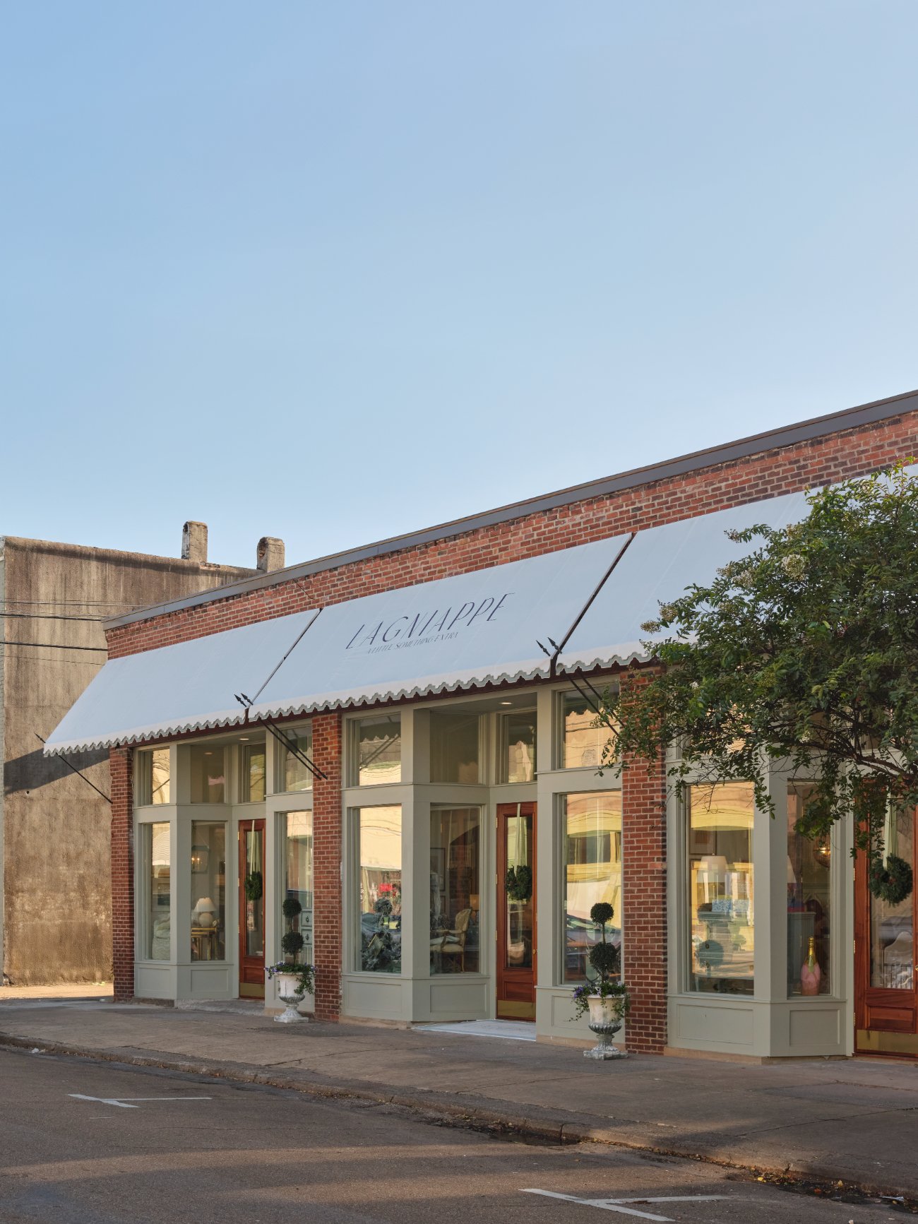 The Lagniappe storefronts in daylight, with a white awning over green-painted wood storefronts and red brick piers