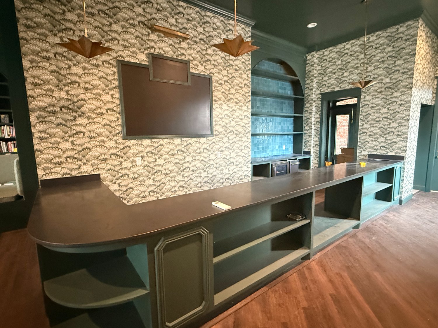 The bookstore's long counter and coffee bar, with patterned wallpaper and brass pendants
