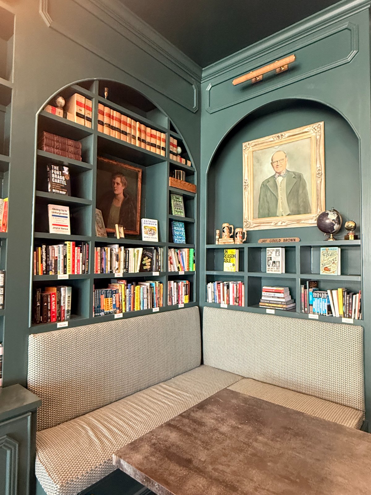 A green-painted reading nook with arched built-in shelving and banquette seating