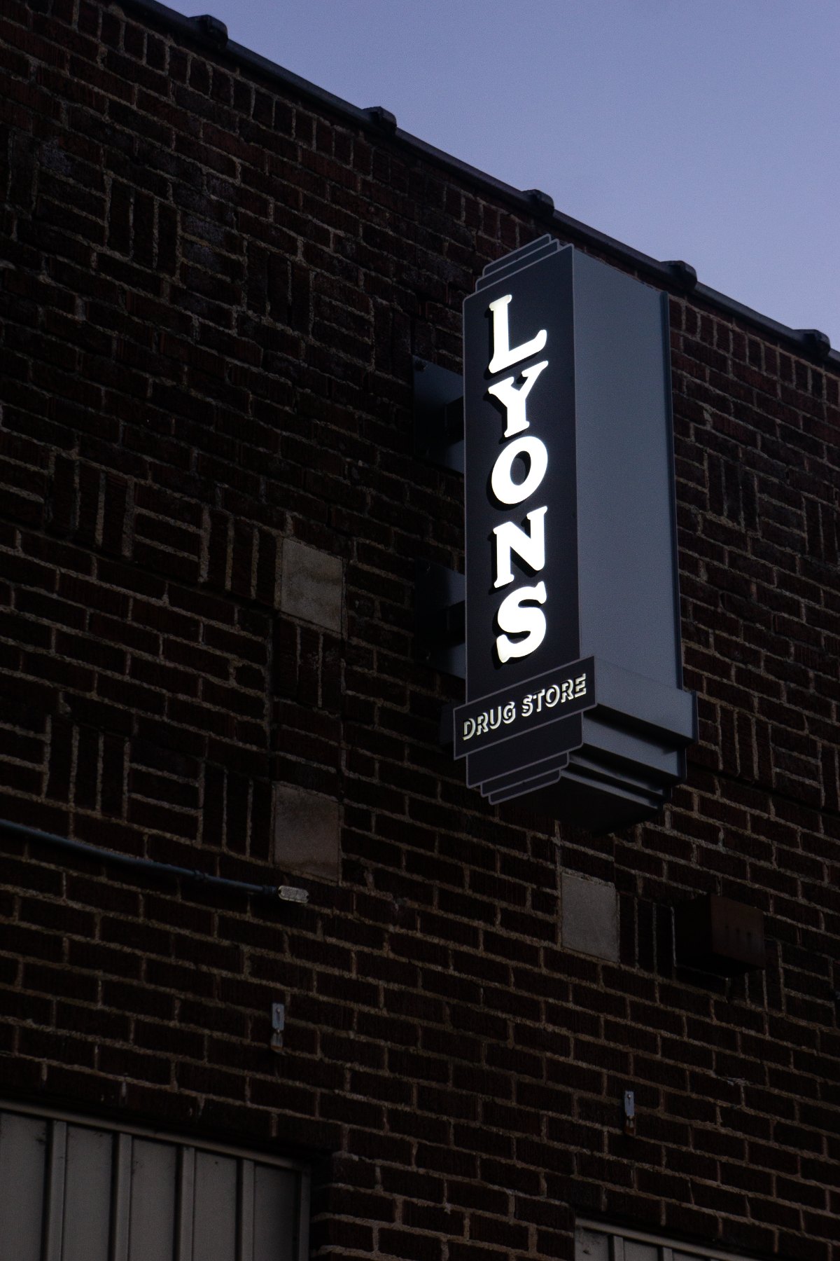 The Lyons Drug Store blade sign lit at dusk